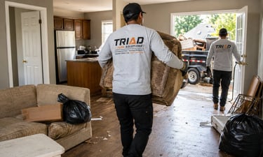 Professional junk removal crew from Triad Junk Solutions carrying old furniture out of a residential home.