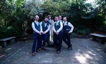 Groom and groomsmen in navy pants and teal vests posing in Abbey Gardens Bury St Edmunds.
