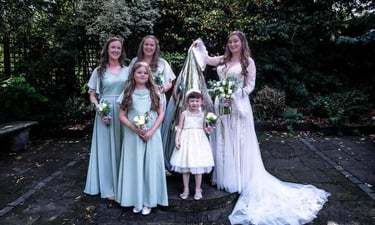 A bride in a white lace gown poses with bridesmaids in Abbey Gardens Bury St Edmunds.