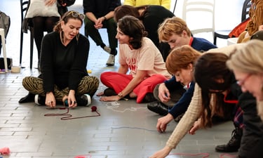 A group of people sitting on the floor drawing their journeys using yarn.
