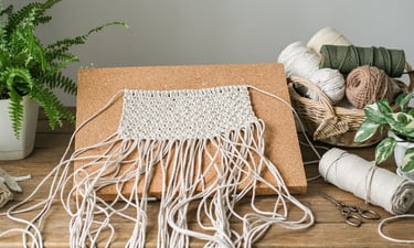 Handmade macrame wall hanging project pinned to a cork board with cotton cord supplies.
