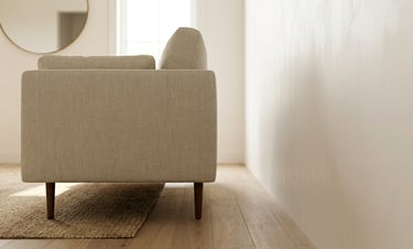 Side view of a modern beige linen sofa on light wood floors in a minimalist living room.