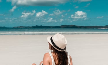 a woman sitting on a beach with a hat on
