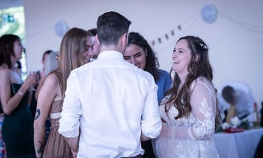 A laughing bride in a lace wedding dress talks to guests during an indoor reception.