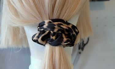 Blonde hair tied in a low ponytail using a trendy leopard print fabric scrunchie on a mannequin head.