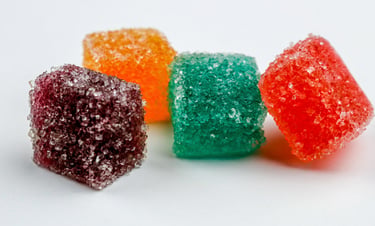 Four colorful fruit flavored sugar coated gummy candy cubes on a white background.