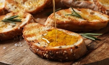 Golden olive oil drizzled over toasted rosemary focaccia bread on a wooden board.