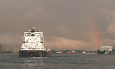 Stern of a black and white freighter as it sails towards a rainbow.