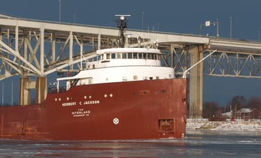 Close-up of the forward pilothouse of a classic red and white freighter passing a bridge.