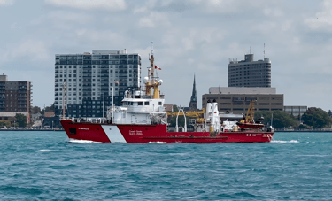 Port side view of red and white Canadian Coast Guard vessel Limnos passing some buildings.