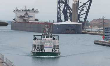 A Soo locks tour boat passes a huge freighter that is pulling into the Poe Lock.
