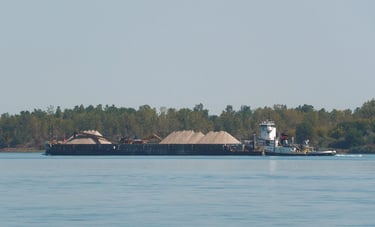 A tugboat pushes a large barge loaded with piles of sand.
