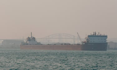 Huge red freighter Stewart J. Cort approaching. The sky is hazy with wildfire smoke.