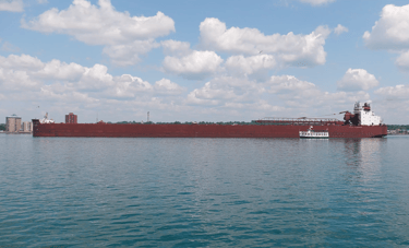 Small Soo Locks tour boat next to huge red freighter James R. Barker.