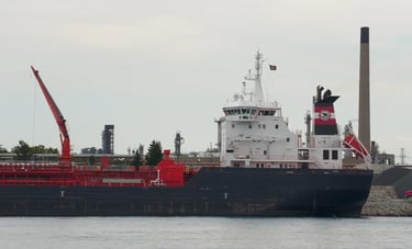 Aft section of a blue and white tanker ship, moored in front of a smokestack.