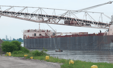 A crewman in a workboat passing by the side of a black hulled freighter.