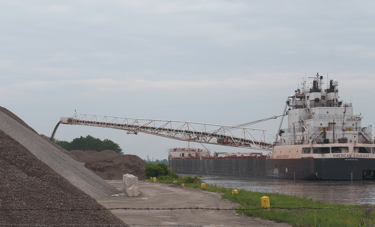 A stern view of freighter American Courage unloading stone onto a large pile.