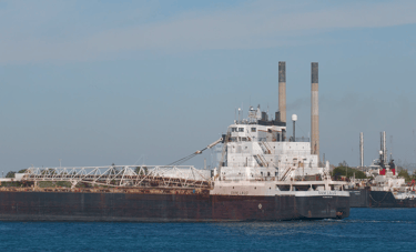 Aft section of a black and white freighter passing 2 smokestacks.