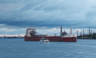A small tour boat passing a large red and white ship under dramatic looking clouds.