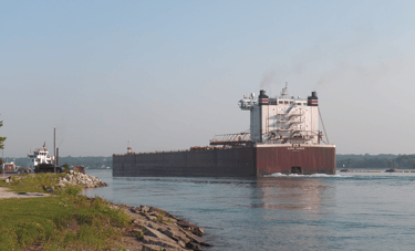 The stern view of a large freighter passing the Sugar Island ferry at Mission Point.