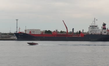 A small fishing boat speeds past a blue tanker ship that is moored.