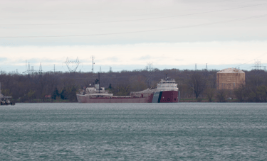 Classic freighter John G. Munson in the distance, Trees and a liquid storage tank in the background.