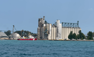 Red and white Canadian Coast Guard vessel Limnos passing grain silos, arriving in Sarnia Harbor.