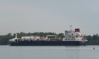 A blue and white tanker ship passing a red buoy with green trees in the background.