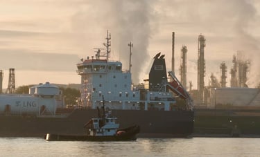 A tugboat passes by the aft section of a tanker ship moored at a refinery.