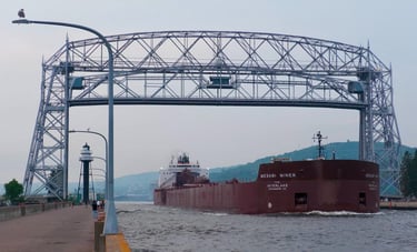A huge red ship passing under the Duluth Aerial Lift Bridge.