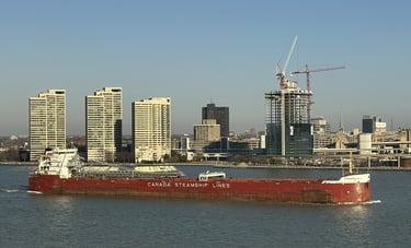 A red and white ship passes by buildings of the Detroit skyline.
