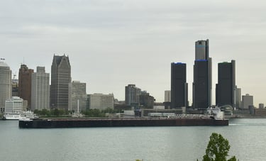 A huge freighter passing downtown Detroit buildings.
