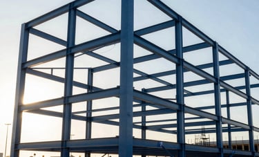Professional photography of the structural steel framework for a large commercial complex under construction in a US city. Sunset lighting creates strong highlights and long shadows on the metal beams. The composition is modern and geometric. Palette: dark blue, light blue, and white.
