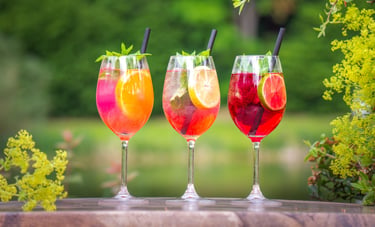Drei bunte Sommer-Cocktails mit Früchten und Minze auf einer Terrasse.