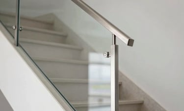 Sleek stainless steel and glass railing installed on a modern indoor staircase. Professional photography showing the precision of the joints and the polished steel surface in a luxury Hispanic / Latin American residential interior.