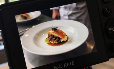 Detailed shot of a professional camera screen displaying a high-contrast photo of a chef plating a dish in a modern kitchen. Soft daylight from a large window in a North American / European setting.