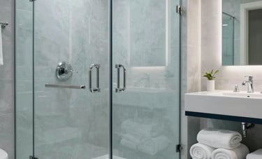 A wide shot of a luxury North American master bathroom after a deep clean. Polished chrome faucets, streak-free glass shower doors, and neatly rolled white towels on a dark navy shelf. The atmosphere is clinical yet welcoming, in shades of light blue and light gray.