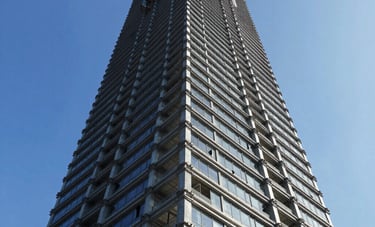 A powerful low-angle perspective of a high-rise building under construction, featuring steel and glass structures against a bright blue sky. High-contrast, dynamic and professional industrial aesthetic.
