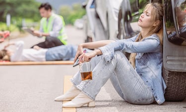 Drunk Driving incident with a woman holding a liquor bottle and sitting against a car after an accident, injured person and e