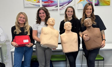 Group of first aid course learners standing with CPR training manikins after completing training