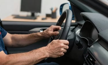 Close-up of a technician's hands detailing a vehicle's interior in a high-end North American residential garage. In the background, a neat desk area suggests professional IT capabilities. Modern, clean aesthetic with steel blue and dark gray accents.