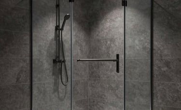 A minimalist walk-in shower with floor-to-ceiling clear glass panels and large format dark gray tiles. A matte black rain shower head and integrated lighting highlight the clean, architectural design in a modern home.