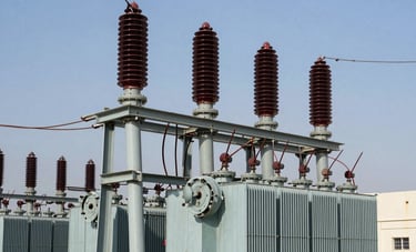 A detailed industrial photograph showing a high-voltage electrical substation in the Middle East. Steel structures, transformers, and complex wiring are captured with precision under professional lighting. The color palette features slate blue and metallic grey tones, emphasizing technical expertise.