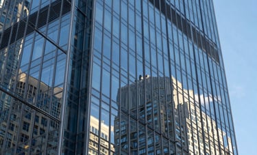A close-up photograph of a modern glass skyscraper reflecting a clear blue sky in a major North American / US financial district. Refined, architectural, and powerful style.