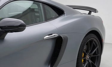 A luxury European sports car in a modern, clean garage environment, showing a flawless application of a satin metallic gray vinyl wrap. The lighting highlights the curves of the vehicle and the premium texture of the foil.