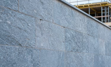 A professional architectural shot of a construction project in Portugal. Focus on a newly built stone wall with clean, modern lines. The scene is bright and highlights the craftsmanship and durability. Blue-grey and light steel blue tones.