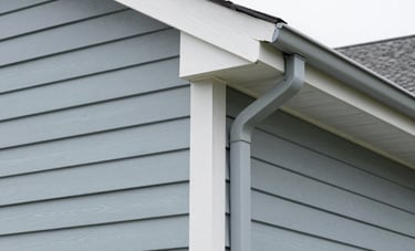 Close-up architectural photography of light blue-gray vinyl siding and seamless gutters on a North American home. Sharp focus, clean lines, professional craftsmanship with muted gray tones.