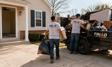 Professional junk removal team loading household debris and old furniture into a Triad Junk Solutions trailer.