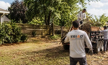 Professional junk removal team loading yard waste and branches into a trailer for debris disposal.