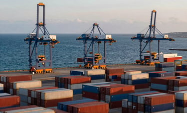 Fotografía de un terminal portuario comercial moderno al atardecer en Latinoamérica. Contenedores de carga apilados frente a un océano azul profundo bajo un cielo despejado. Calidad profesional.